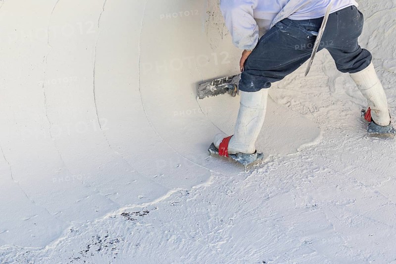 Worker wearing spiked shoes smoothing wet pool plaster with trowel