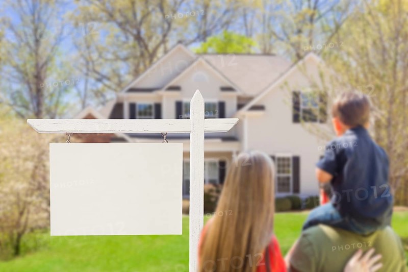 mixed-race young family in front of blank real estate sign and new house