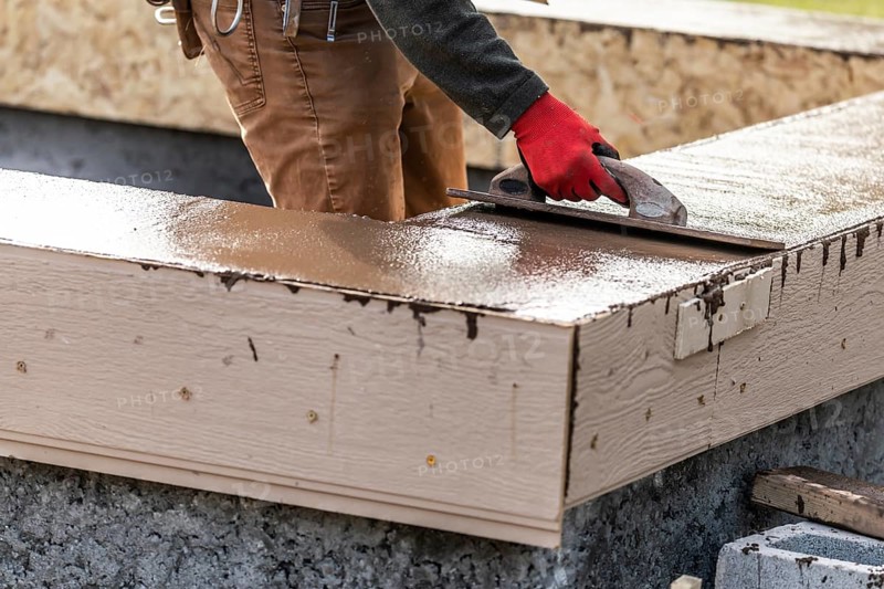 Construction worker using wood trowel on wet cement forming coping around new pool