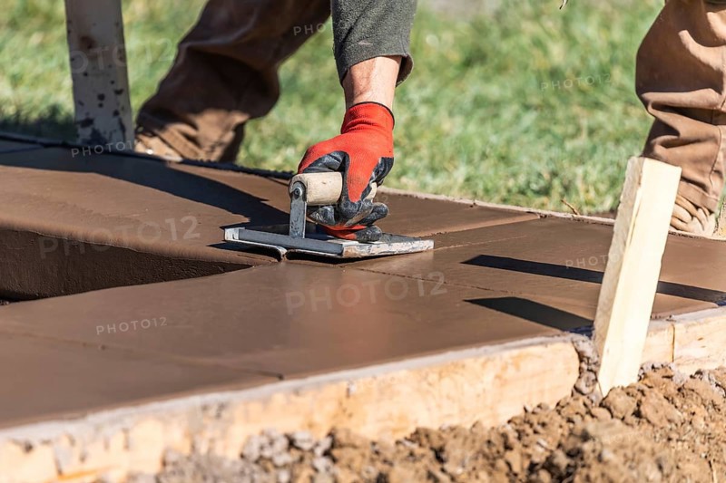 Construction worker using hand groover on wet cement forming coping around new pool