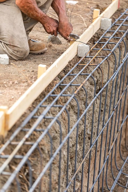 Worker securing steel rebar framing with wire plier cutter tool at construction site