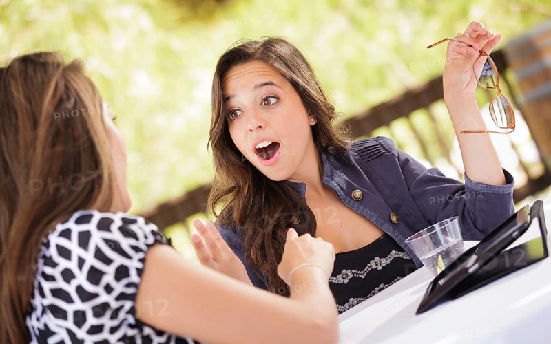 Expressive young adult girlfriends using their computer electronics outdoors