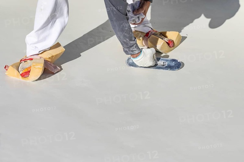 Worker wearing sponges on shoes smoothing wet pool plaster with trowel