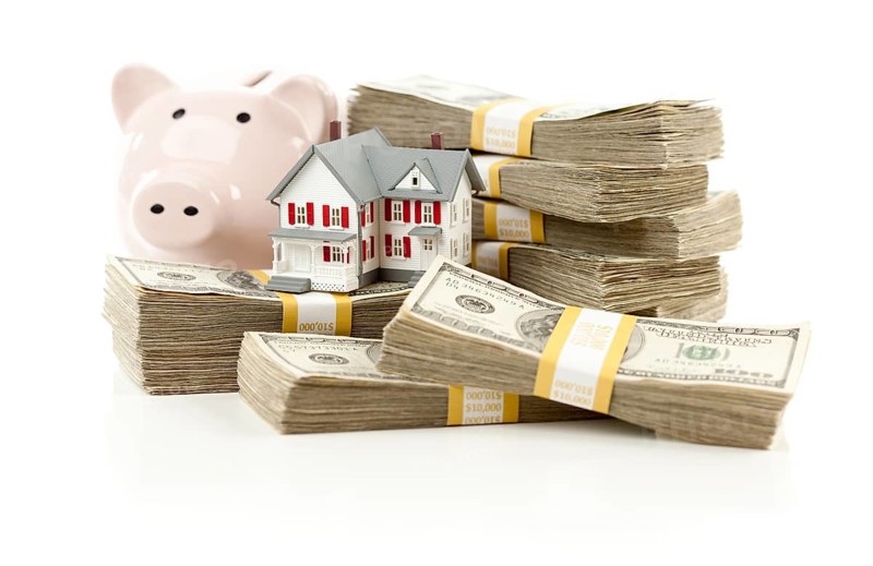 Small house and piggy bank with stacks of hundred dollar bills isolated on a white background