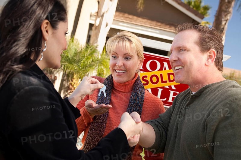 Hispanic female real estate agent handing over new house keys to excited couple