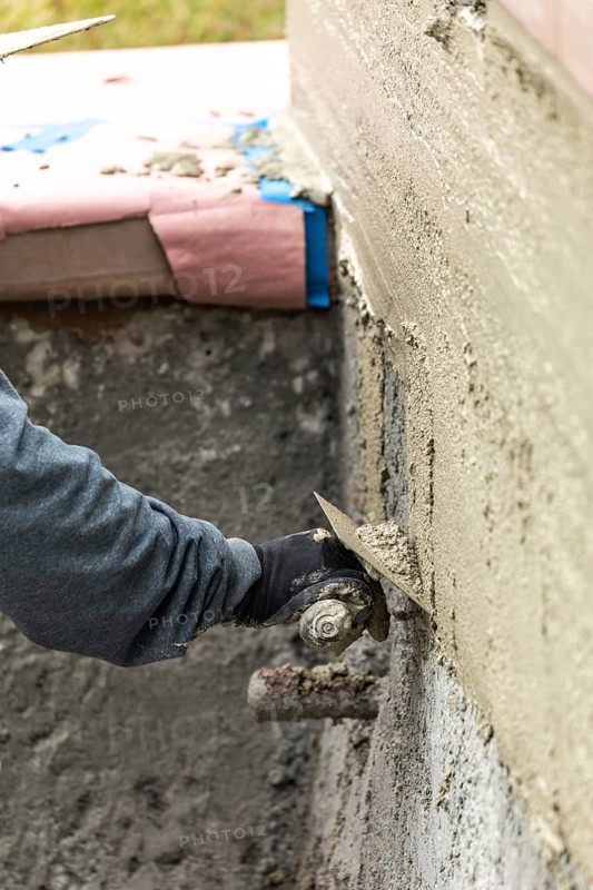 Tile worker applying cement with trowel at pool construction site