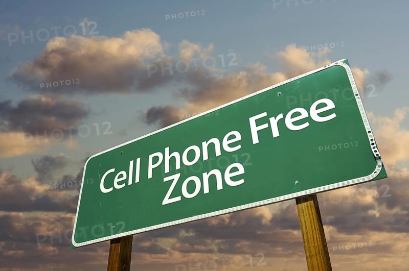 Cell phone free zone green road sign in front of dramatic clouds and sky