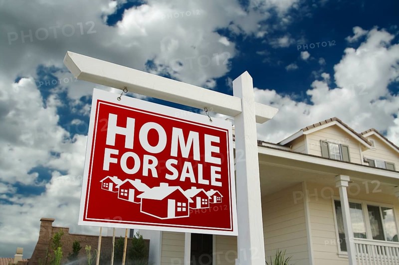 Red home for sale real estate sign and house against a blue sky