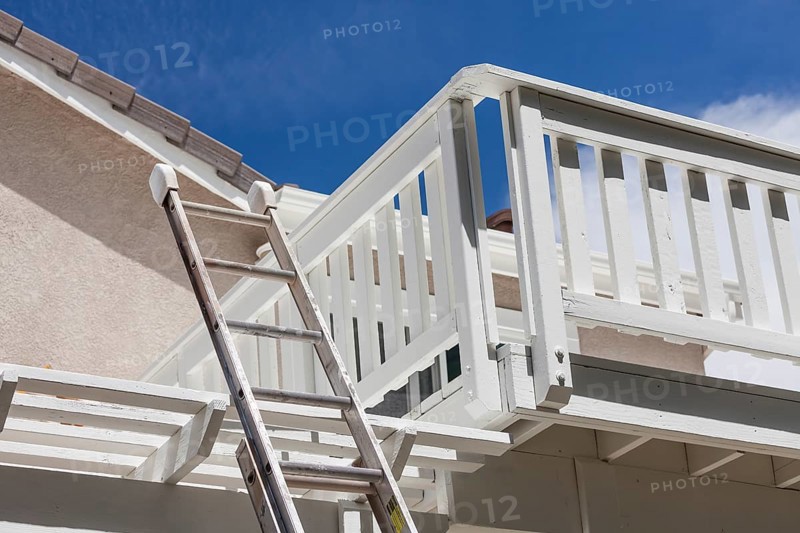 Construction ladder leaning on white house deck with blue sky behind