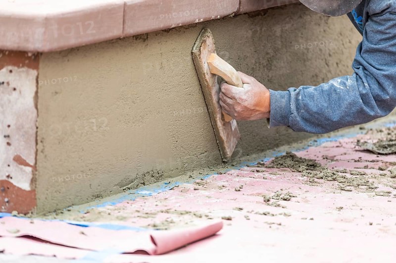 Worker smoothing cement with wooden float at construction site