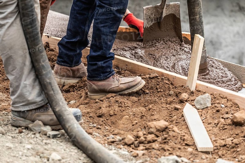 Construction workers pouring and leveling wet cement into wood framing