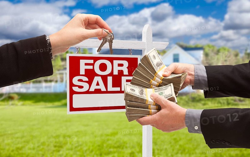 Man handing woman thousands of dollars for keys in front of house and for sale real estate sign