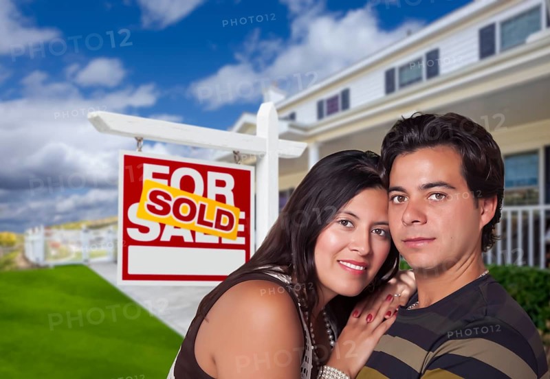Young happy hispanic couple in front of their new home and sold for sale real estate sign