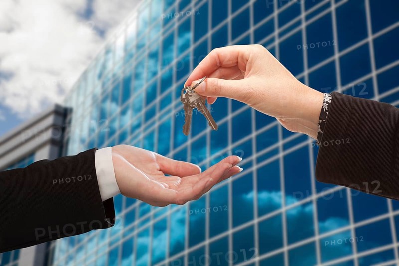 Female handing over the keys to other woman in front of corporate building