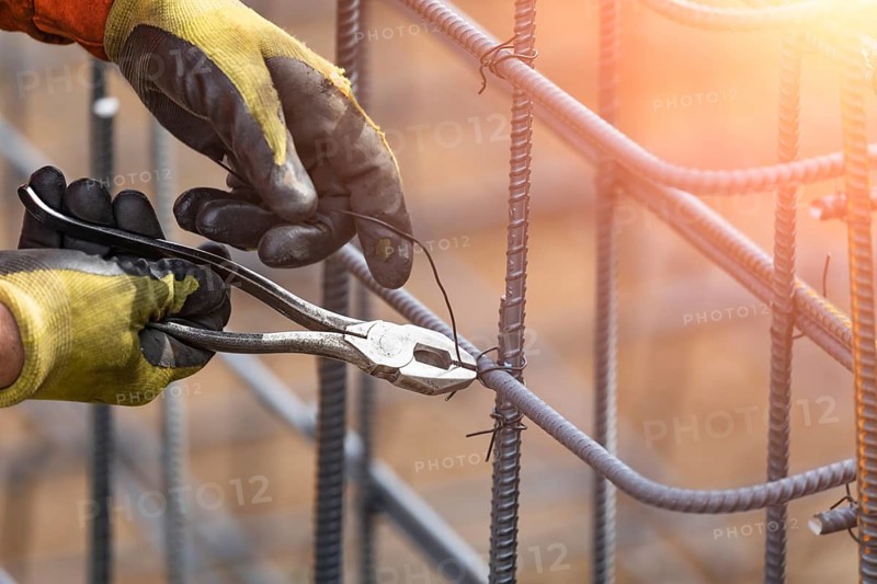 Worker securing steel rebar framing with wire plier cutter tool at construction site