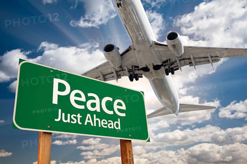 Peace green road sign and airplane above with dramatic blue sky and clouds