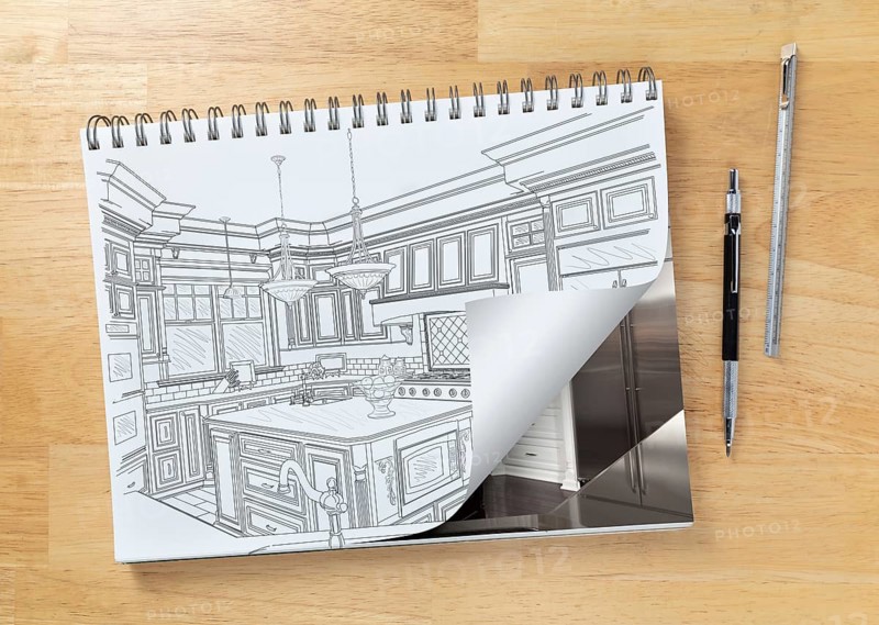 Sketch pad on desk with drawing of custom kitchen and page corner turning to show finished construction next to engineering pencil and ruler scale