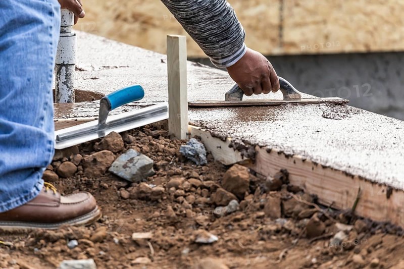 Construction worker using wood trowel on wet cement forming coping around new pool