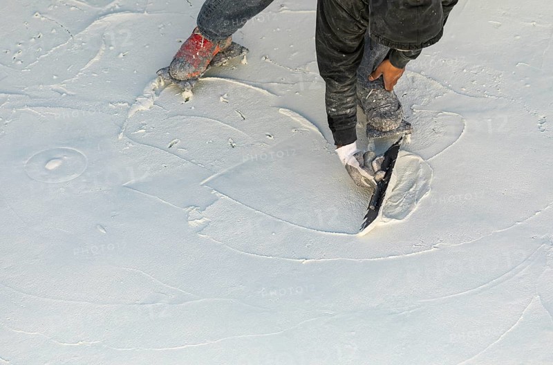 Worker wearing spiked shoes smoothing wet pool plaster with trowel
