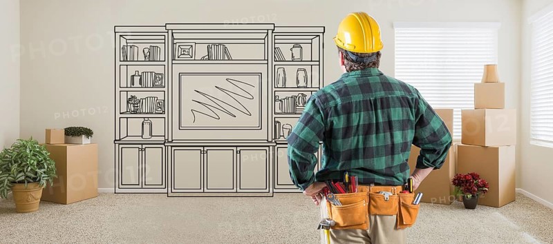 Contractor inside room with boxes facing entertainment unit drawing on wall