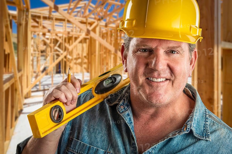 Smiling contractor in hard hat holding level and pencil at construction site