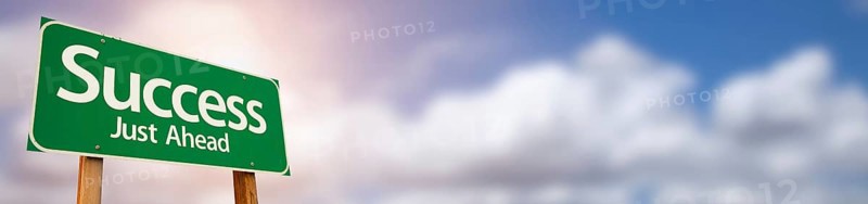 Success green road sign wide banner with room for text against clouds and sunburst