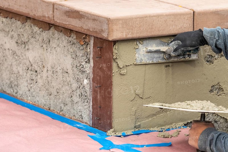Tile worker applying cement with trowel at pool construction site