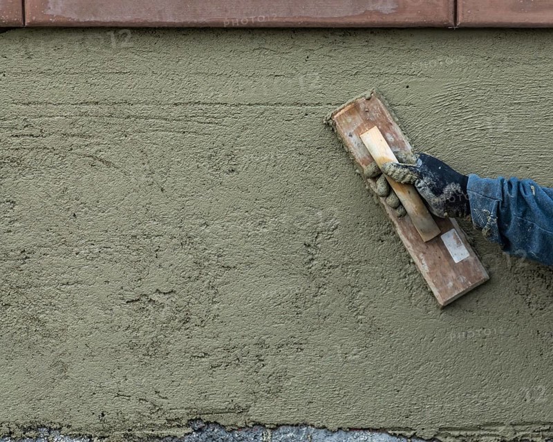 Worker smoothing cement with wooden float at construction site