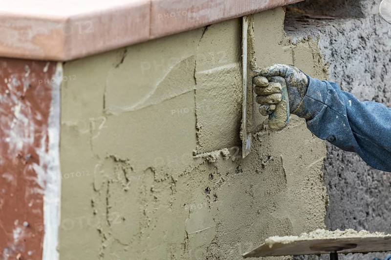 Tile worker applying cement with trowel at pool construction site