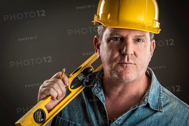 Serious contractor in hard hat holding level and pencil with dramatic lighting