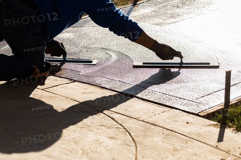 Construction worker smoothing wet cement with trowel tools