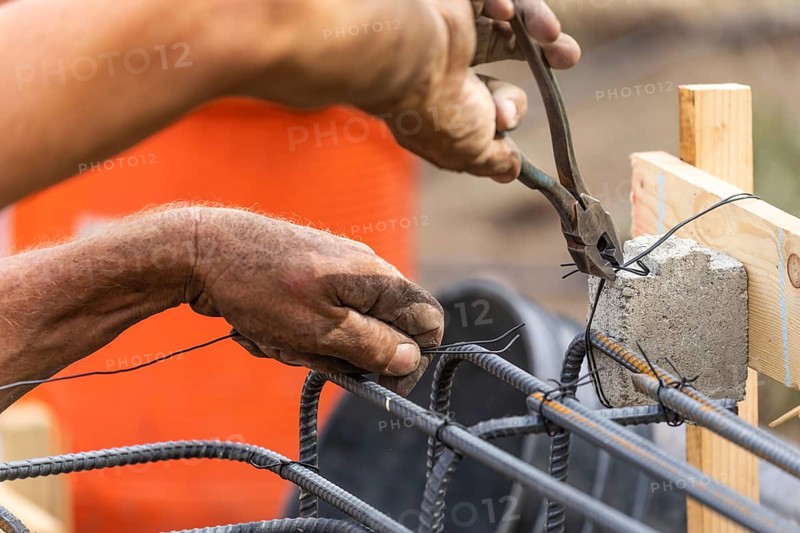 Worker securing steel rebar framing with wire plier cutter tool at construction site