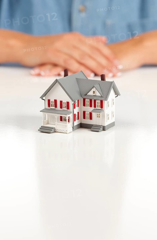 Womans folded hands behind model house on white surface