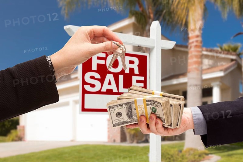 Agent handing over keys as buyer is handing over cash for house with home and for sale real estate sign behind