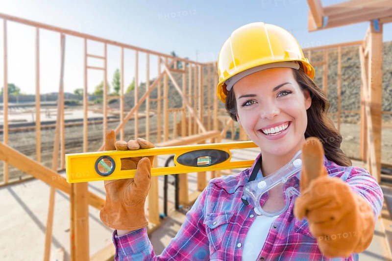 Female construction worker with thumbs up holding level wearing gloves