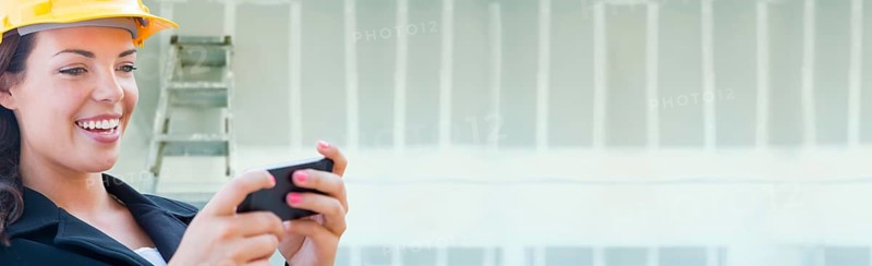 Female contractor wearing hard hat using cell phone against dywall banner background with ladder
