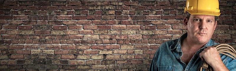 Male contractor in hard hat holding cable in front of old brick wall banner with copy space