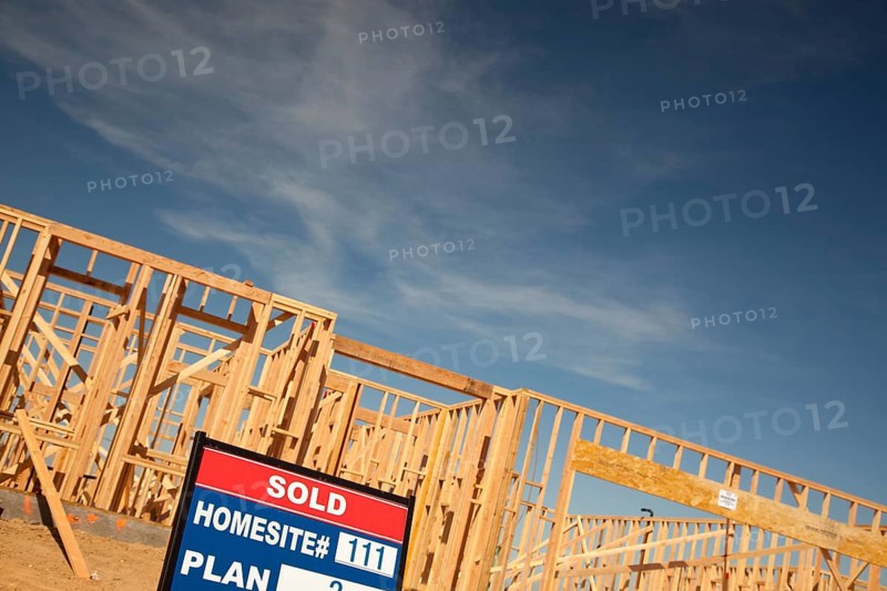 Sold lot real estate sign at new home framing construction site against deep blue sky