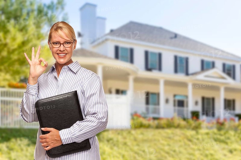 Attractive businesswoman with okay hand sign in front of nice residential home