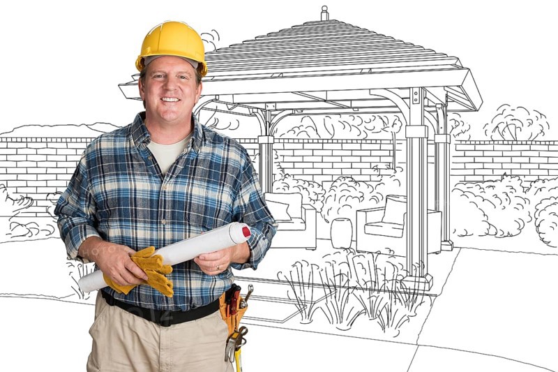 Male contractor with house plans wearing hard hat in front of custom pergola patio covering drawing