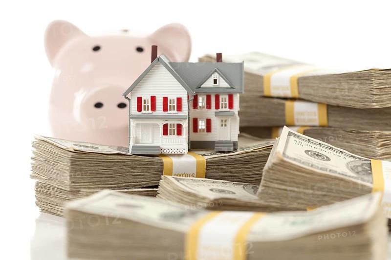 Small house and piggy bank with stacks of hundred dollar bills isolated on a white background
