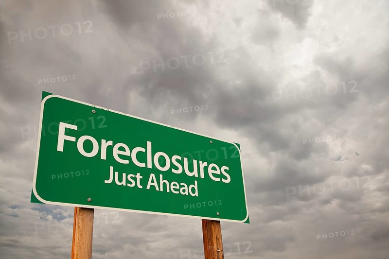 Foreclosures just ahead green road sign with dramatic storm clouds and sky
