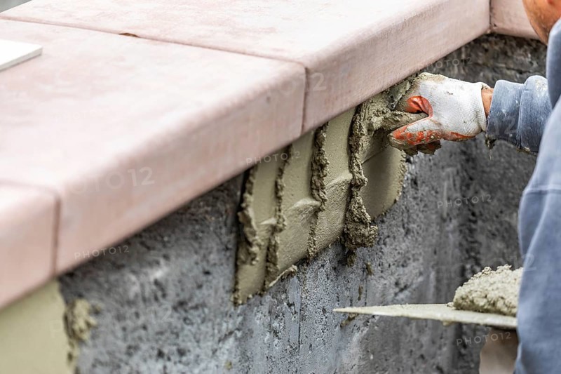 Tile worker applying cement with trowel at pool construction site