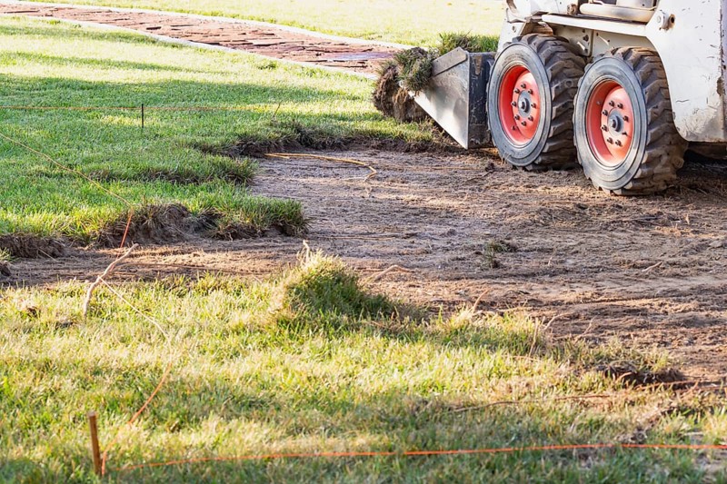 Small bulldozer removing grass from yard preparing for pool installation