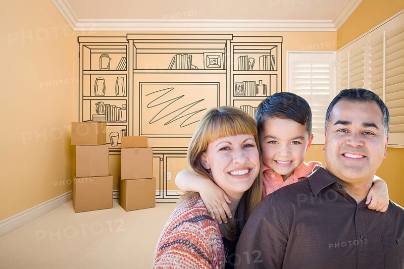 Happy young mixed-race family in room with moving boxes and drawing of entertainment unit on wall