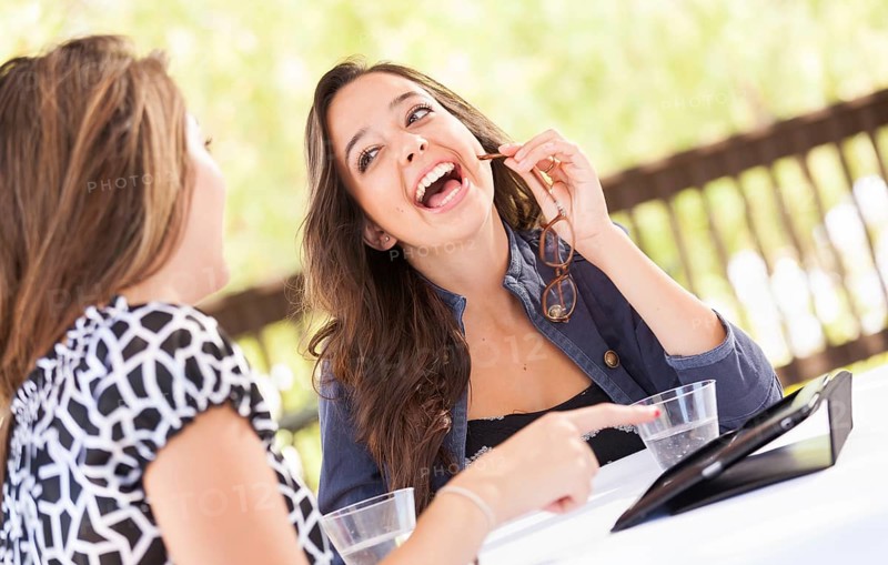 Expressive young adult girlfriends using their computer electronics outdoors