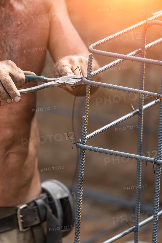 Worker securing steel rebar framing with wire plier cutter tool at construction site