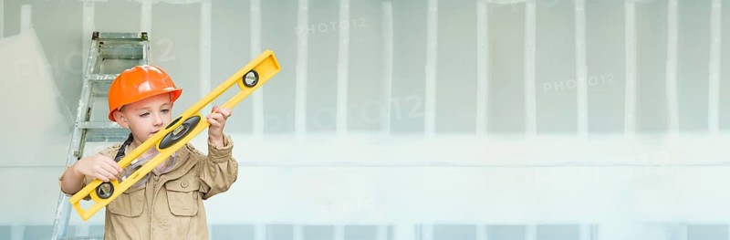 Cute young boy dressed as contractor holding level against dywall banner background with ladder
