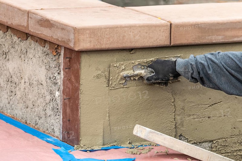 Tile worker applying cement with trowel at pool construction site