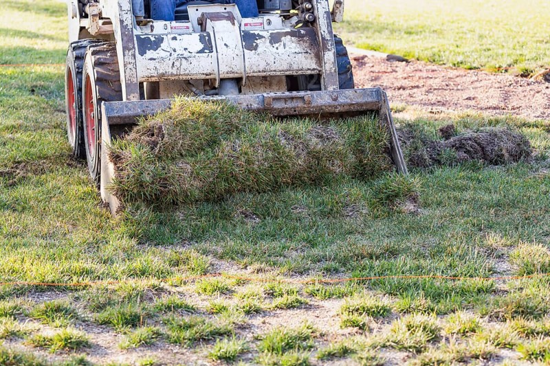 Small bulldozer removing grass from yard preparing for pool installation